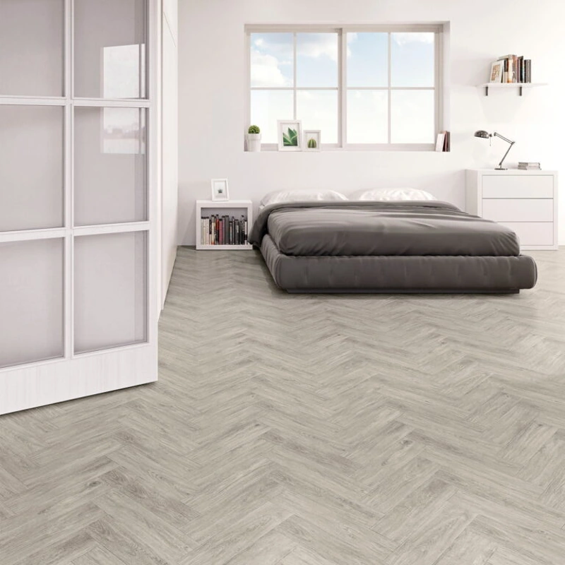 Light-toned herringbone laminate flooring with subtle wood grain texture.